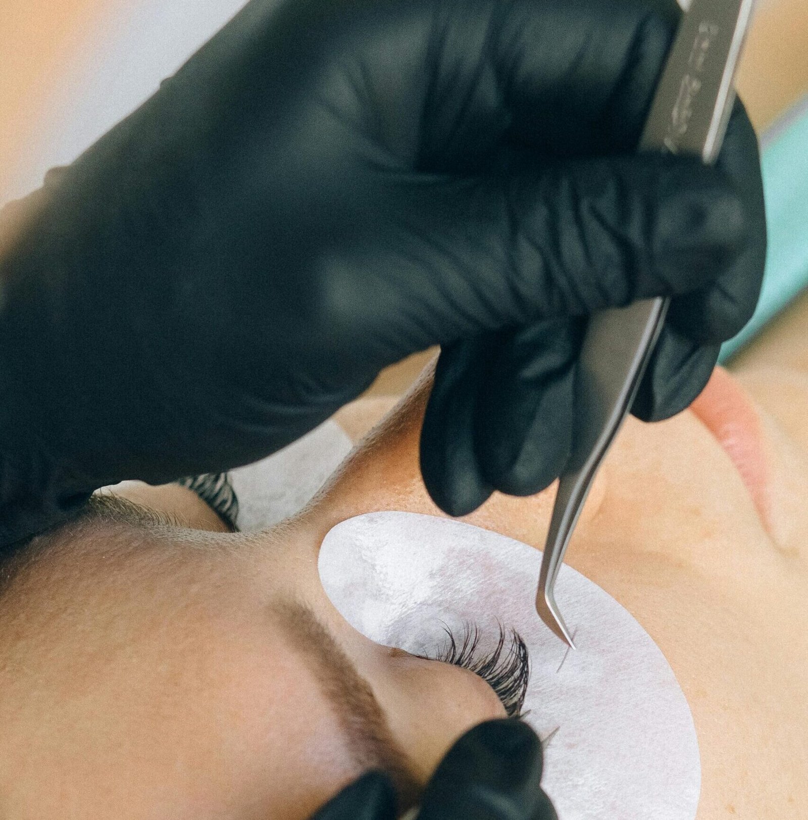 Close-up of eyelash extension application with black gloves and tweezers.